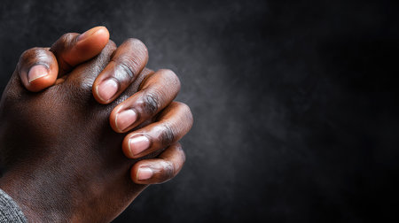 This image showcases a close-up of clasped hands with dark skin tone against a black background. The hands, with visible veins and neatly trimmed nails, exhibit a warm, brown hue. The composition highlights texture and form with soft lighting. Suitable for projects related to faith, prayer, spirituality, or contemplation.の素材