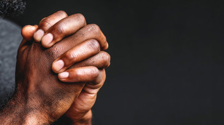 This image showcases a close-up of clasped hands against a dark backdrop. The hands, with visible skin texture, are the central focus. The composition includes ample copy space. This visual could be suitable for various uses, including editorial content and design projects, particularly those themed around faith or contemplation.の素材