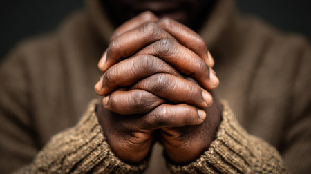 The image features a close-up of a person's hands clasped together, suggesting prayer or contemplation. The hands, with their dark skin tone, are the central focus. The textured surface of the person's clothing provides a contrast with the hands. This composition might be useful for projects related to faith, spirituality, or introspective themes.の素材