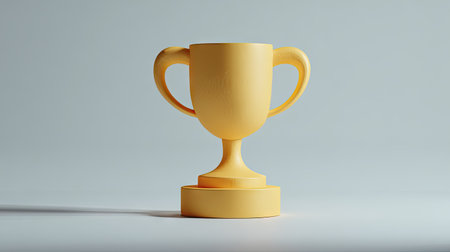 A golden trophy cup stands prominently against a light gray backdrop. The image showcases the cup's form with smooth surfaces and balanced composition. The lighting highlights the object, suggesting a studio setting. This visual is suitable for illustrations about success, awards, or achievements in various industries.の素材