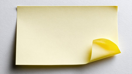 A single yellow sticky note is shown, featuring a curled corner against a white background. The composition is simple with soft lighting, and it appears to be captured with a close-up perspective. This image could be used in various commercial or editorial contexts to represent concepts such as planning, reminders, or messages.の素材