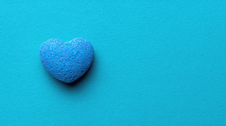 A single, textured blue heart rests on a flat turquoise surface in this close-up shot. The heart shape dominates the composition, offering a soft texture. The lighting appears diffused, emphasizing the object's form. This image could serve various purposes including design elements or illustrations.の素材