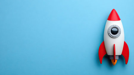 A vibrant rocket ship model is positioned against a solid blue backdrop. The object features a white body with red fins and nose cone. This studio shot showcases a clean design with bright colors. Suitable for illustrating ideas related to space, exploration, business, or technology, this image has ample copy space.の素材