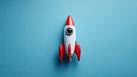 A close-up studio shot showcases a toy rocket ship. The model features red fins and a nose cone set against a clear blue backdrop. Its design is clean and simple. The image could be used for various projects, including advertising or educational materials.の素材