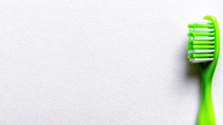 A close-up view presents a green toothbrush with white and green bristles, placed against a textured white backdrop. The composition is simple, with the toothbrush positioned on the right side. The image showcases bright colors and a clean aesthetic. This image is suitable for health and wellness related media.の素材