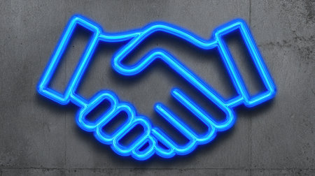 A vibrant neon blue handshake icon is displayed on a textured concrete surface. The illuminated graphic symbolizes collaboration and partnership. The composition uses high-contrast lighting and a simple, graphic style. Suitable for illustrating business concepts, teamwork, or corporate communication. It may be used in various commercial or editorial applications.の素材