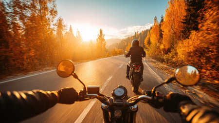 Two motorcycles ride along a paved road. The image captures a first-person perspective with handlebars in focus. Golden sunlight bathes the scene, illuminating autumn foliage along the road. The photo suggests motion, travel, and adventure, suitable for various commercial uses.の素材