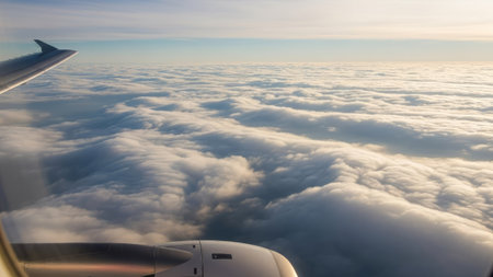 An aerial view from an airplane window depicts a sea of clouds illuminated by daylight. The image showcases the wing of the aircraft and the engine against the vast, fluffy white cloud formation. This scene illustrates travel and can be used for various commercial or editorial projects related to aviation or weather.の素材