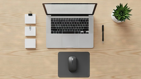 An overhead shot depicts a workspace featuring a laptop, mouse, and stationery arranged on a wooden desk. The composition shows natural lighting emphasizing the various textures and colors. This image is suitable for a range of uses, including website design, advertising material, and business presentations.の素材