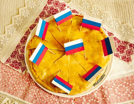 Russian pie cut into eight pieces lying on a platter with patriotic flagsの写真素材