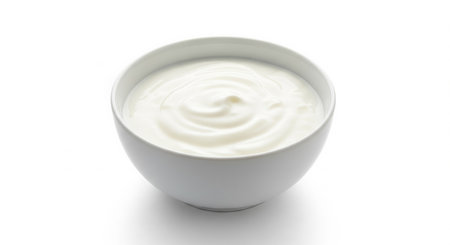 A metal spoon lifts dense glossy yogurt from a white ceramic bowl with morning light creating gentle highlights across the smooth surfaceの素材