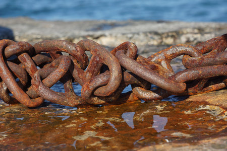 a fragment of a rusty chain on a concrete pier at the seaside