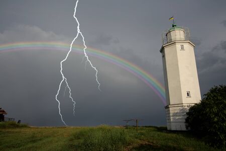 Rainbow against a lighthouse after a thunder-storm with lightning flashの写真素材