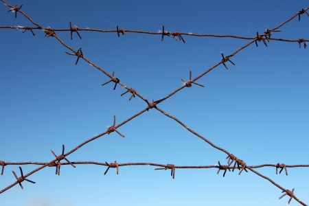 Barbed wire tense on a fence against the blue skyの写真素材