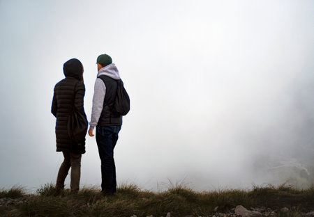 Back view of two young people looking at the foggy mountain landscapeの写真素材