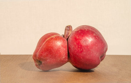 Two red apples on a wooden table with a beige background.