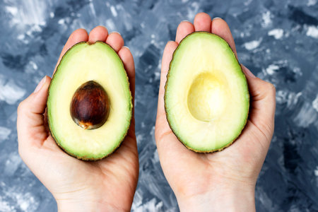 Female hand holds avocado close-up, top view