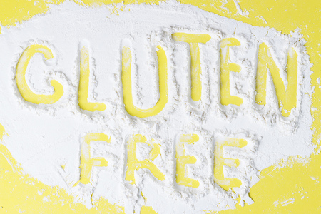 A scattered flour on a yellow background with the inscription Gluten Freeの写真素材