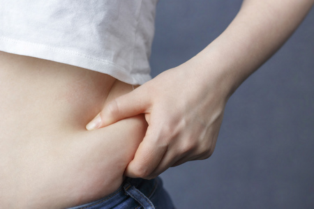 A woman's hand holding excessive belly fat, the concept of weight lossの写真素材