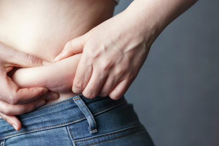 A woman's hand holding excessive belly fat, the concept of weight lossの写真素材