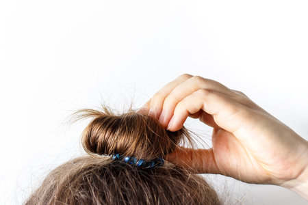 Female hand correct the bun on a white background. Modern fast hairstyle.