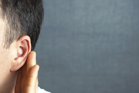 The man listens attentively with her palm to her ear, close up, the news conceptの写真素材