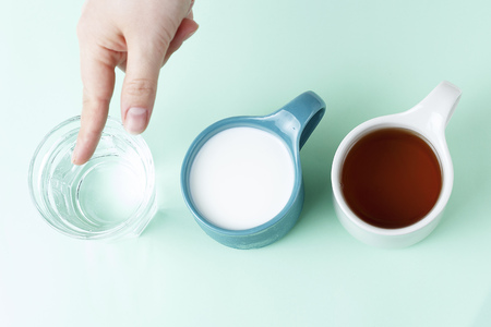 Multicolored mugs with hot drinks and a female hand on a blue background, top viewの写真素材