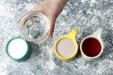 Multicolored mugs with drinks and a female hand on a gray background, top viewの写真素材