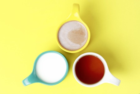 Milk, tea and hot chocolate in colorful circles on a yellow backgroundの写真素材