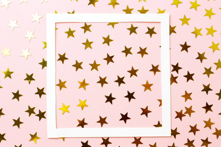 A golden confetti and white frame on a pink background, top view