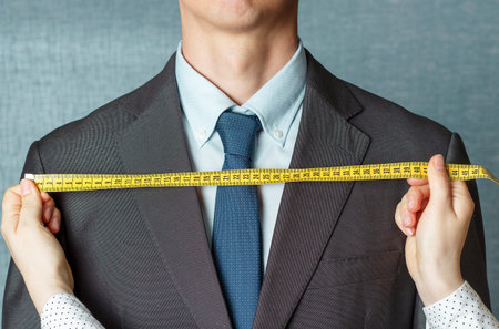 The tailor measures the suit with a measuring tape close up