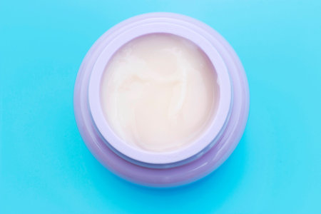 Jar with white cream on blue background, a top view, copy space