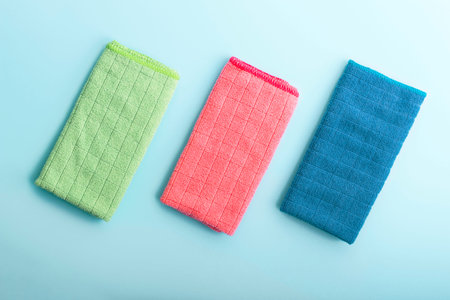 Three multi-colored microfiber rags on a blue background, concert cleaning.