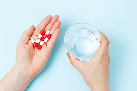 Female hand holding a glass of water and pills, top view