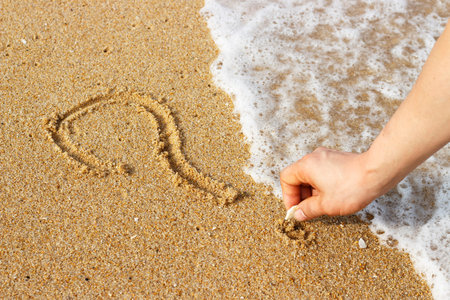 Male hand draws on sand question mark, a top view