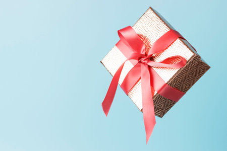 Gold color gift box with pink ribbon on blue background close up, copy space. Levitation