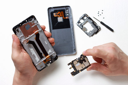 Men's hands hold a screwdriver in their hands and repair a broken smartphone