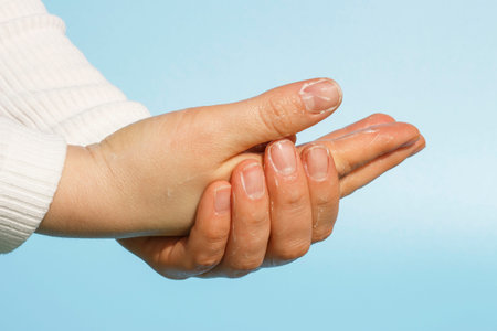 Girl washes her hands with soap close up on a blue background.