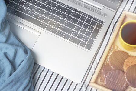 A laptop and a wooden tray with cookies on the bed top view, concert freelance.の写真素材