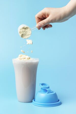 Female hand pours Shaker protein on a blue background, side view.の写真素材