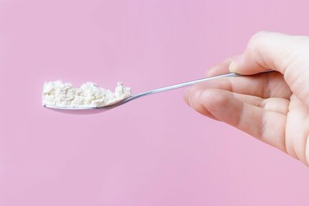 Female hand holds a teaspoon with collagen on a pink background, side view.の写真素材