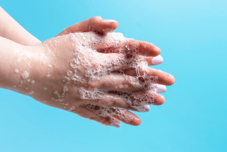 Girl carefully washes her hands with soap close-up on a blue background.