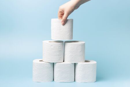 Female hand stacks toilet paper in a stack on a blue background close-up.の写真素材