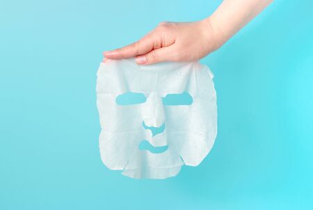 Female hand hold a fabric mask on a blue background.の写真素材