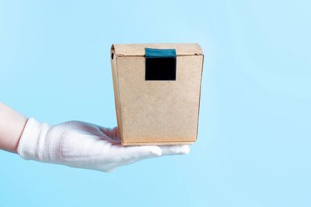 A woman's hand in a glove holds a cardboard box with food, the concept of food deliveryの写真素材