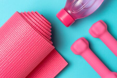 Sports mat, pink dumbbells and a bottle of water on blueの写真素材