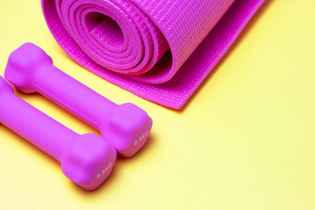 Pink sports mat and dumbbells on yellow background, a copy of the space