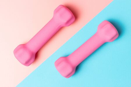 Pink dumbbells on a pink and blue background, top view, sports backgroundの写真素材