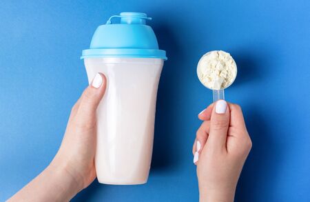 Female hands with white manicure hold a bottle of protein shake and a measuring spoon with protein powder, top viewの写真素材