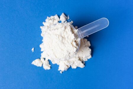 Scattered protein powder and scoop on a blue background, top viewの写真素材